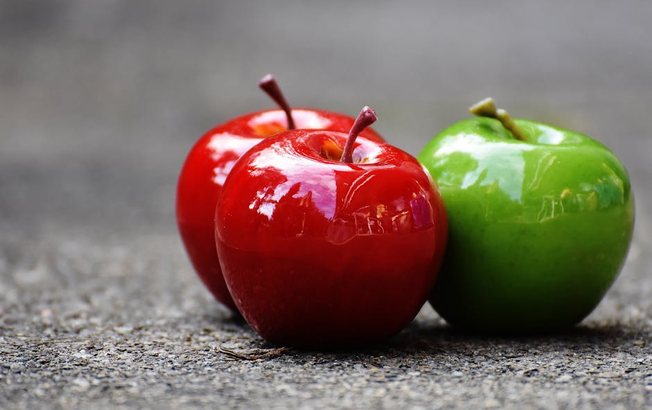 Close-up of shiny red and green apples on a textured surface, showcasing freshness and vibrant colors.